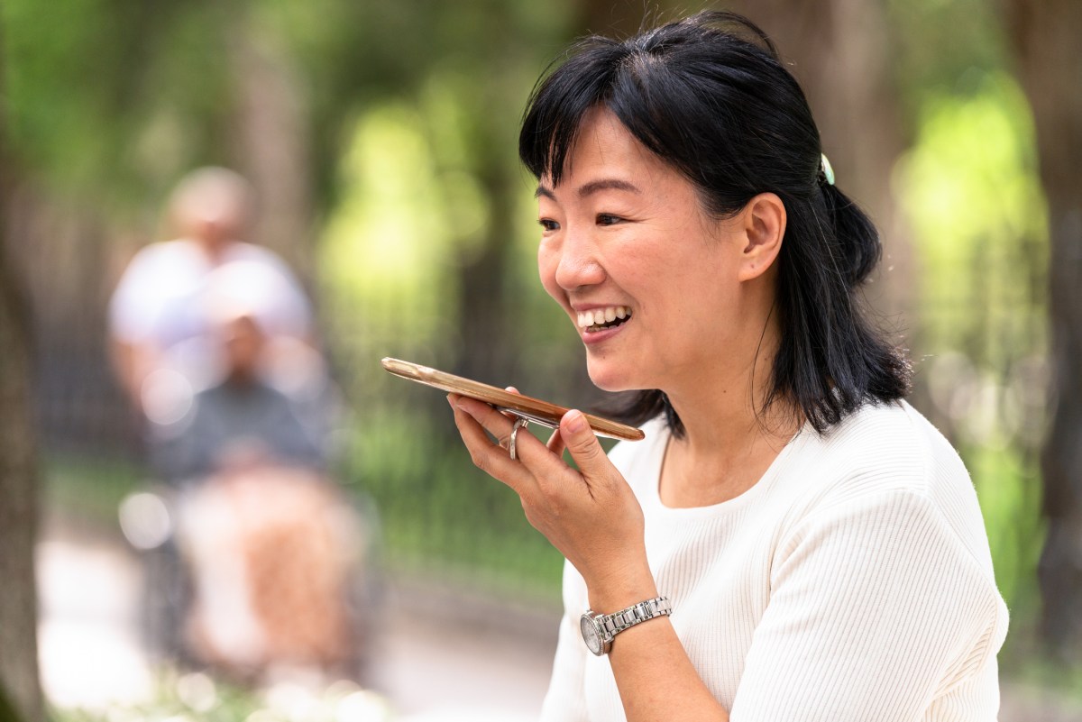 A woman using the speakerphone on her smartphone during a call in a Taipei park.